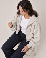 AI-generated model Maya seated in the unzipped light gray Everyday Zip Hoodie, holding a drawstring
